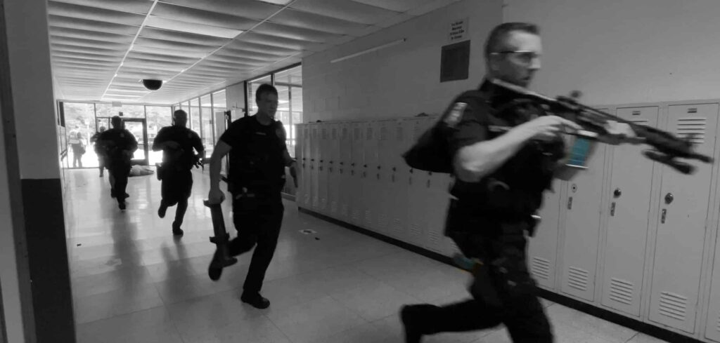 Grayscale photo of police officers with rifles advancing down a hallway during an active shooter training drill.