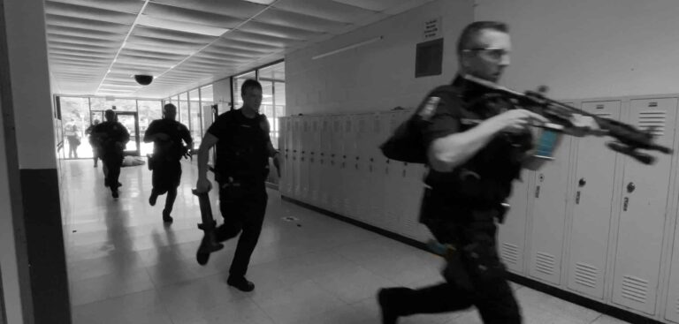 Police Response Training – Mass Shooting Protocol PDF for City Leaders | Scenario Trainer Active Shooter Response Training Systems | Scenario Trainer Active Shooter Response Training Systems Grayscale photo of police officers with rifles advancing down a hallway during an active shooter training drill.